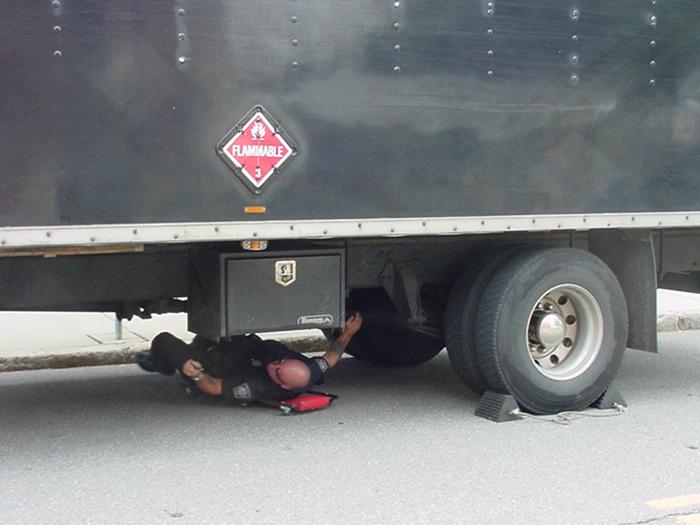 A police officer inspecting the bottom of a truck.