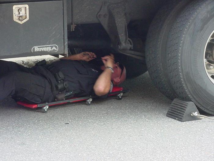 A police officer inspecting the bottom of a truck.